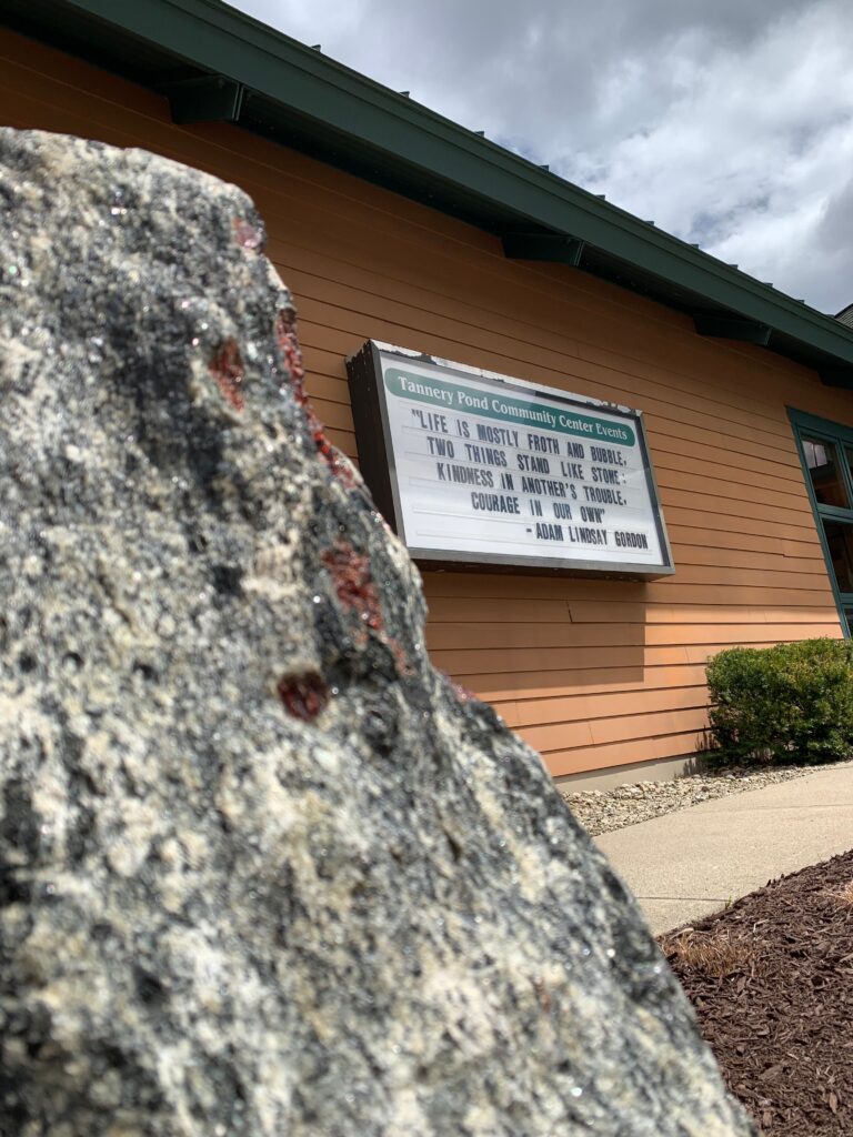 A granite slab sits in the foreground of a sign for Tannery Pond Community Center.