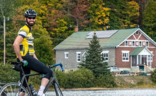 Guy on a bike smiling at the camera with a brick building in the background
