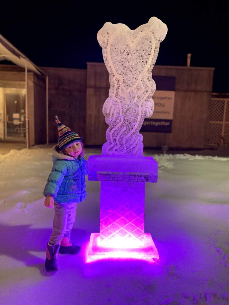 Little kid standing next to an ice sculpture lit up with purple/pink lights