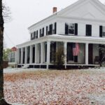 White building with American Flag hanging on the porch, snowy grass