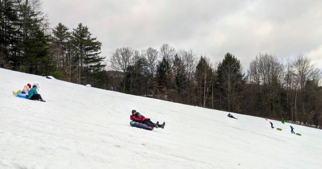 A few kids slide down a snowy hill.
