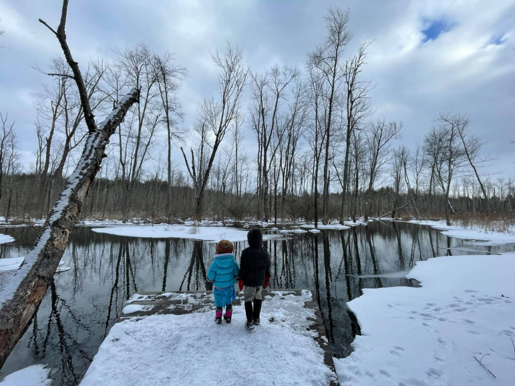 two kids standing on a snowy deck looking towards the water