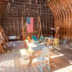 Inside of building with picnic tables, Adirondack chairs, and an American flag hanging on a wooden wall